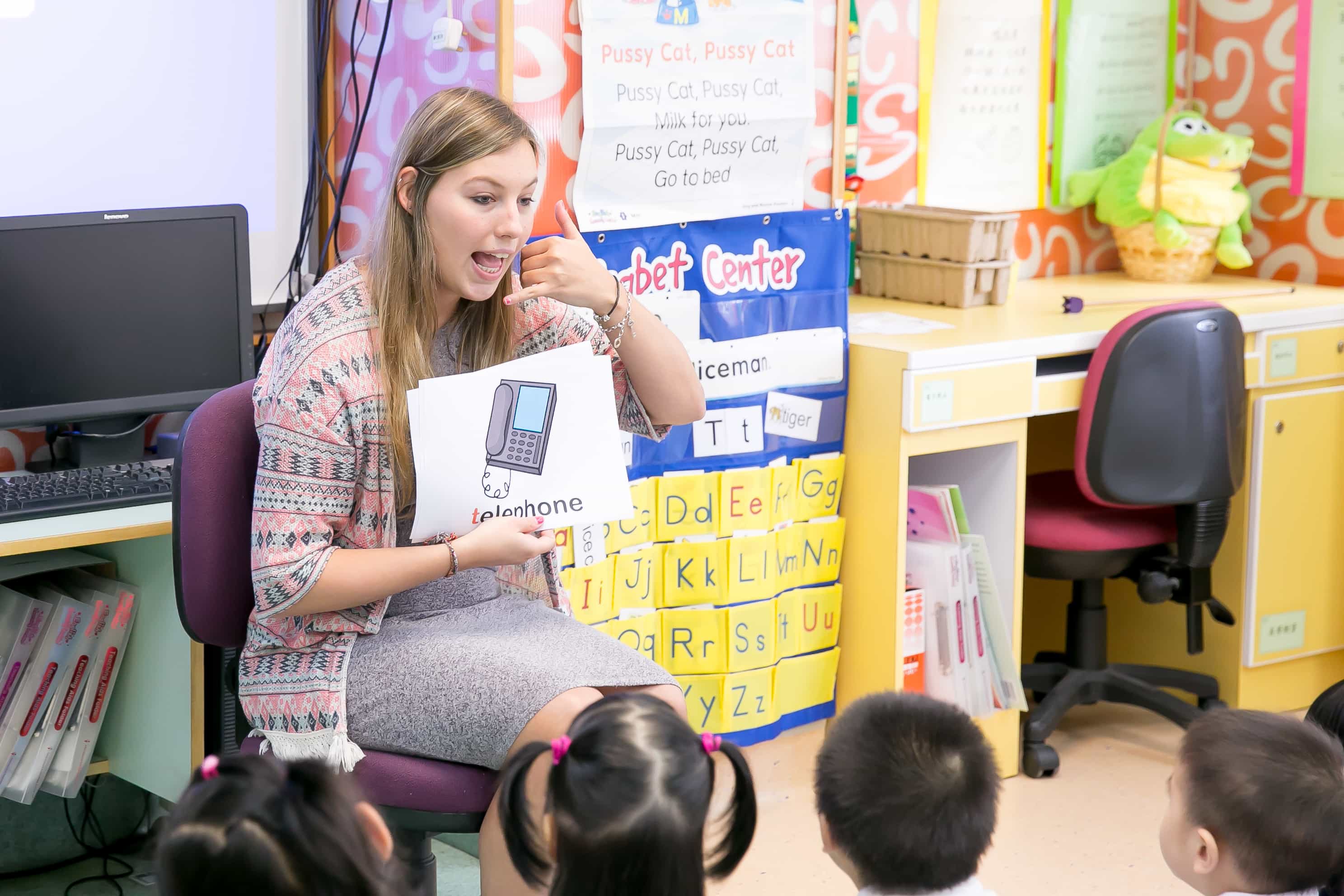 a TEFL teacher in the classroom explaining children the word telephone